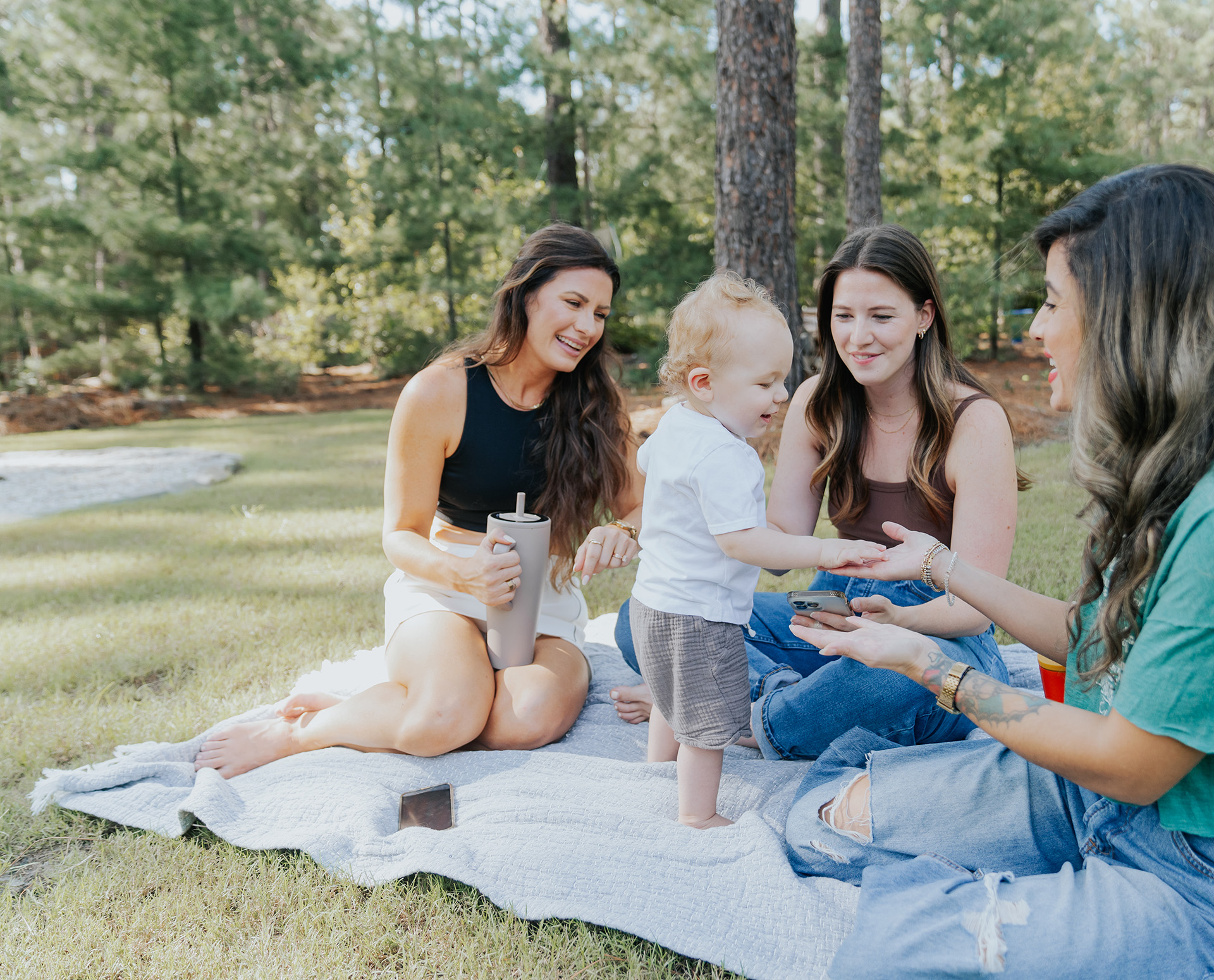 Group of people sitting in the park playing with a child.